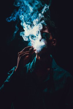 Siyah Gözlüklü Genç Adam Siyah Arkaplanda Dumanlı Puro İçiyor.