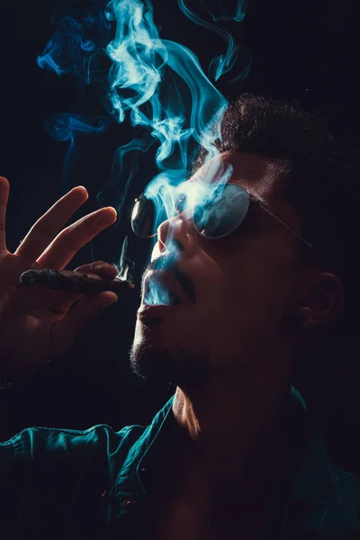 stock image Black Young Man with Glasses Smoking Cigar with Fog at Black Background, low key light.