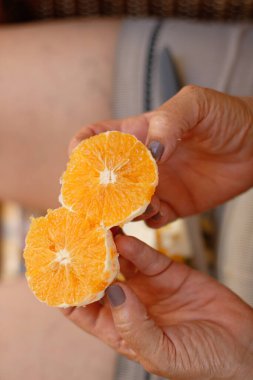 Portakal dilimini iki parçaya ayıran olgun bir kadın oturmuş meyve yiyor.