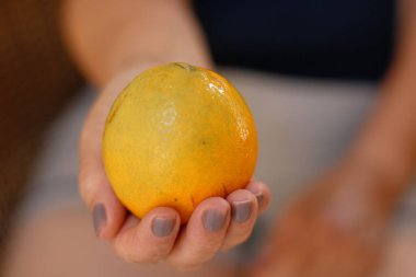 Portakal dilimini iki parçaya ayıran olgun bir kadın oturmuş meyve yiyor.