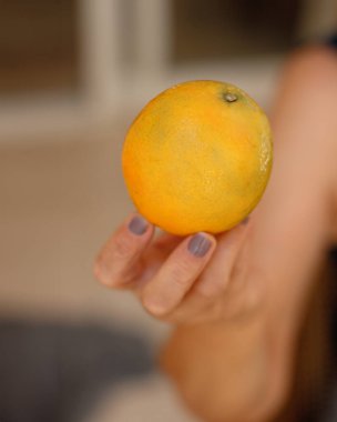 Portakal dilimini iki parçaya ayıran olgun bir kadın oturmuş meyve yiyor.