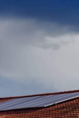 Güneşli ve bulutlu bir günde kırmızı çatıdaki güneş panelleri. 