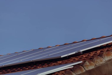 Güneşli ve bulutlu bir günde kırmızı çatıdaki güneş panelleri. 