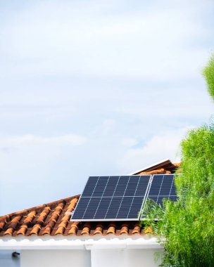 Güneşli ve bulutlu bir günde kırmızı çatıdaki güneş panelleri. 