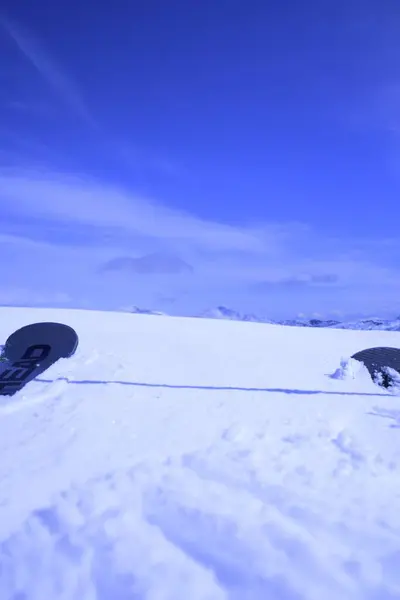 Arka planda açık mavi bir gökyüzü olan, karlı bir yüzeyde dinlenen bir snowboard 'un yakın plan görüntüsü. Kar bakir ve el değmemiş, sakin bir kış manzarası yaratıyor..