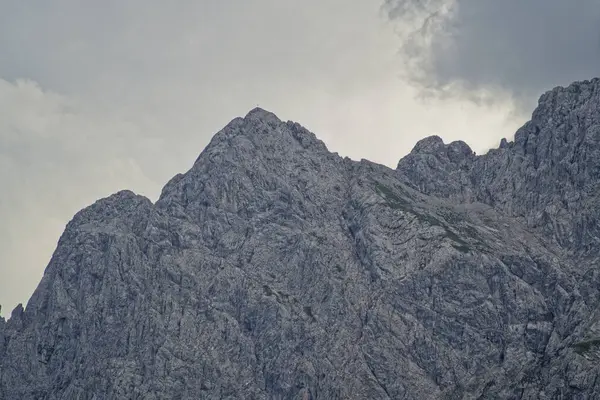 Bulutlu bir gökyüzünün altındaki engebeli dağların yakın görüntüsü. Kayalık yüzeyler detaylı, dağların doğal dokularını ve oluşumlarını gösteriyor..