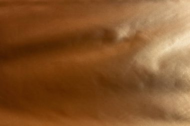 Pürüzsüz, parlak ve hafif desenli kahverengi bir kumaşın yakın plan görüntüsü. Kumaşın sıcak, altın-kahverengi bir tonu ve ince renk ve doku değişiklikleri vardır. Yüzey yumuşak ve lüks görünüyor..