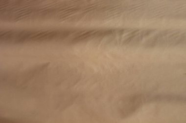 Pürüzsüz, parlak ve hafif desenli kahverengi bir kumaşın yakın plan görüntüsü. Kumaşın sıcak, altın-kahverengi bir tonu ve ince renk ve doku değişiklikleri vardır. Yüzey yumuşak ve lüks görünüyor..