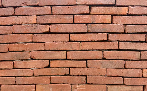 Kırmızı tuğlalı bir duvarın yakın plan görüntüsü. Tuğlalar zengin, kırmızımsı kahverengi, doku pürüzlü ve düzensiz..