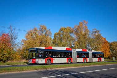 Prag, Çek Cumhuriyeti - 28 Ekim 2024 - Güneşli bir günde yolcularla dolu modern uzun tramvay. Arka planda sonbahar ağaçları.