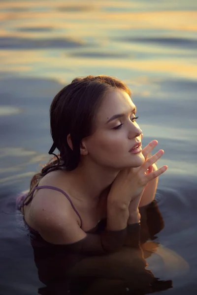 Beautiful young woman in lake water in summer dress at sunset. Portrait of a romantic wet girl at sunset, warm sun, natural beauty of a woman