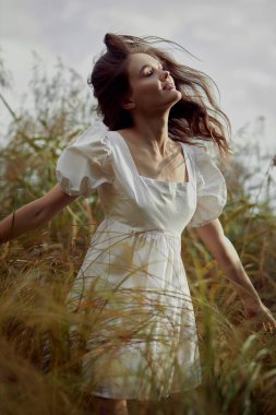 Tarladaki uzun otların arasında romantik genç bir kadın. Beyaz elbiseli, rüya gibi kibar bir kadın. Doğal güzellik, hayatın keyfi.