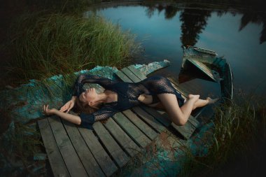 Güzel romantik bir kadın göl kenarında oturuyor. Gün batımında güneşin altında iç çamaşırlarıyla ıslak bir kadın. Doğal güzellik, uzun saç.