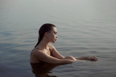 Güzel romantik bir kadın göl kenarında oturuyor. Gün batımında güneşin altında iç çamaşırlarıyla ıslak bir kadın. Doğal güzellik, uzun saç.