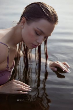 Güzel romantik bir kadın göl kenarında oturuyor. Gün batımında güneşin altında iç çamaşırlarıyla ıslak bir kadın. Doğal güzellik, uzun saç.