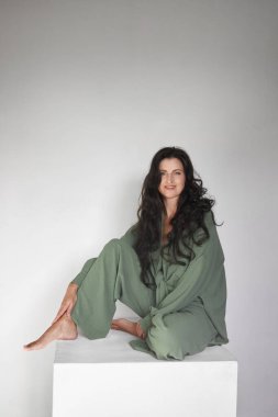 Stüdyoda beyaz küpün üzerinde oturan mutlu kadın. Portre mutlu kadın, kameraya bakıyor, uzun saçlı.