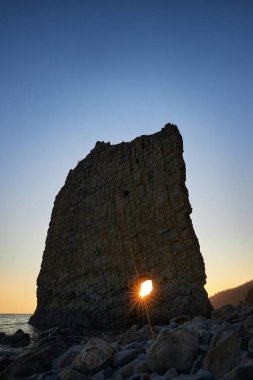 Güneş ufkun altına batıyor, kayalık kıyı şeridi, doğa güzelliği huzur içinde. Dalgalar yavaşça kıyıya vururken, siluetli kayalıklar, koyu gökyüzüne karşı görkemli bir şekilde duruyor.