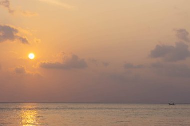 Gün batımı, ufukta tek bir tekne otururken okyanusu sıcak renklerde yıkar.