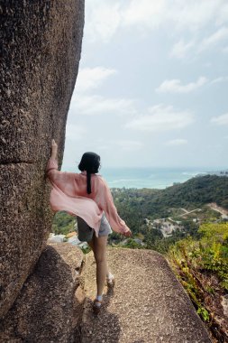 Bir kadın bir uçurumun kenarında durur, sırtını kameraya çevirir, okyanus manzarasını ve manzarayı seyreder..