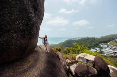 Koh Samui kıyısına bakan bir tepede büyük bir kayanın yanında duran bir kadın. Ada arka planda görülebilir, güneşin altında parlayan okyanusun turkuaz sularıyla..