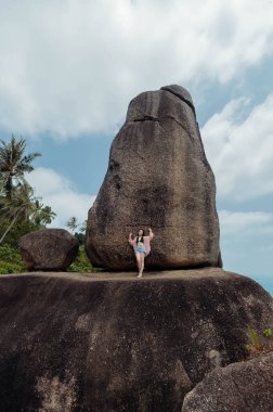 Bir kadın büyük bir kayanın üzerinde duruyor ve başka bir devasa kaya oluşumuna bakıyor. Kayalıklar, Koh Samui, Tayland 'da popüler bir turizm merkezi olan Hin Ta Hin Yai olarak bilinir..