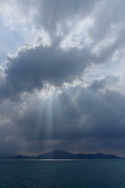 Sakin bir an, güneş ışınlarının dramatik bulutların arasından geçerek sakin denizi ve uzak dağları aydınlatarak barışçıl bir doğal atmosfer yaratmasıyla başlar..