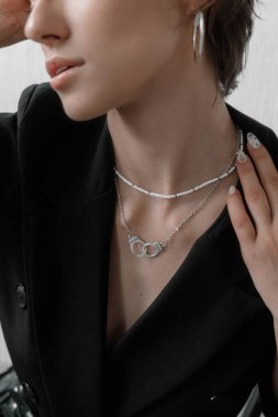 Genç bir kadın siyah ceketinin üzerinde zarif bir şekilde çeşitli gümüş kolyeler sergiliyor, eşsiz tarzını ön plana çıkarıyor..