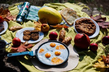 Konforlu piknik düzenlemelerinde kızarmış yumurtalı bir tava, elma gibi taze meyveler ve güneşli bir günde ışıl ışıl sonbahar yapraklarının arasına yerleştirilmiş çeşitli fırınlanmış yiyecekler sergileniyor..