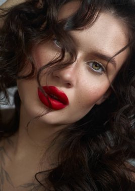 Kadın dalgalı siyah saçlarıyla omuzlarının üzerinden geçiyor, koyu kırmızı dudaklarını ve büyüleyici yeşil gözlerini parlaklaştırıyor. yumuşak ışıklandırma onun doğal güzelliğini ve zarafetini arttırır..