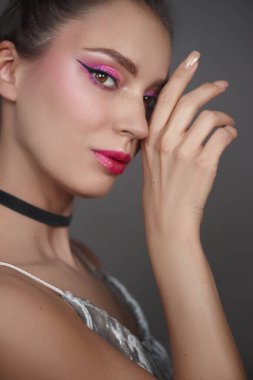 Kendine güvenen bir model, bir eli yüzünün yanında zarif poz verirken canlı pembe aksanlarıyla çarpıcı makyajını sergiliyor. Pürüzsüz saç stili genel görünüşü ve havayı tamamlıyor..