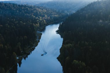 Küçük bir tekne kıvrımlı bir nehirde sessizce dolaşırken, canlı sonbahar yaprakları, sabahın erken saatlerindeki yumuşak güneş ışığının altında orman kıyılarına tutunuyor..