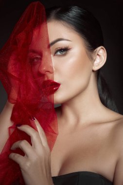 Stüdyoda koyu bir geçmişi olan bir kadın elinde saf kırmızı bir kumaşla dikiliyor. Cesur kırmızı dudakları, büyüleyici makyajı, kendine güveni ve cazibesi var..