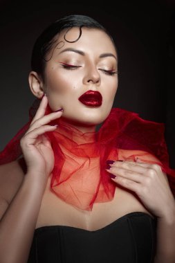 Model, gözleri kapalı, çarpıcı kırmızı ruj ve makyajla zarifçe poz verir. Boynunda saf kırmızı atkı perdeleri, dramatik ve sofistike bir görünüm yaratıyor..