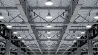 Yüksek tavanlar ve açığa çıkmış metal kirişlerle endüstriyel bir depoyu aydınlatan parlak yukarıdaki ışıklar. 3d hazırlayıcı.