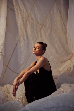 Gösterişli siyah elbiseli bir kadın zarif bir şekilde oturur yumuşak, örtülü bir arka plana..