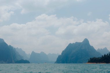 Sakin sular uzak bir yerdeki görkemli dağları yansıtıyor. Tepelerin katmanları gün içinde huzur ve doğal güzelliği çağrıştırıyor..