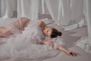 Yumuşak ışık filtreleri, açık bir yüzeyde zarif bir şekilde uzanan ve akıcı, desenli bir elbise giyen bir model gibi katıksız kumaştan geçer. Atmosfer sakin ve sanatsal..