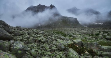 Kayalık arazi, bulutların tepelerin üzerinde yakın uçtuğu sisli bir dağ manzarasında görülebilir. Öğleden sonra ortalık sakin ve sakin..