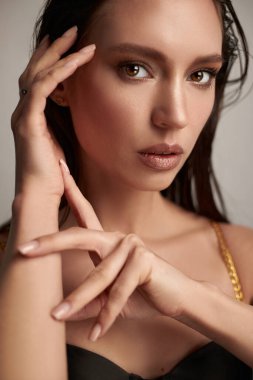 Model zarif bir ifadeyle zarifçe poz veriyor, tarafsız bir zemine karşı onun özelliklerini ve zarafetini vurguluyor. Ellerine ve yüz detaylarına odaklanıyor. Gelişmişliği çağrıştırıyor..