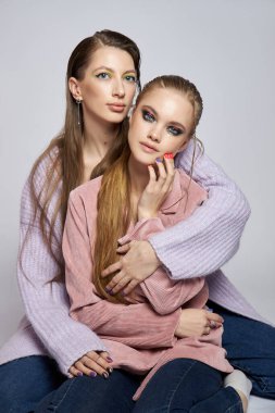 İki arkadaş bir stüdyoda poz verirken aynı sevgi dolu anı paylaşıyorlar. Tarafsız bir arkaplanda canlı makyaj stilleri sergiliyorlar, bağlantılarını ve bireysel kişiliklerini vurguluyorlar..