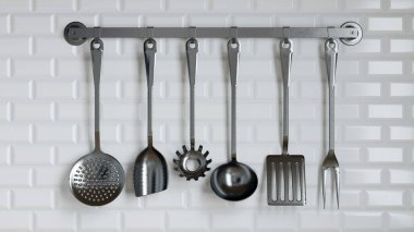 Pürüzsüz metal mutfak aletleri koleksiyonu, dokulu beyaz bir duvara karşı bir askıda sergilenmekte ve yemek pişirme ve hazırlama için çeşitli araçlar sergilenmektedir. 3d hazırlayıcı