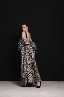 Model, göz alıcı bir leopar desenli bir elbiseyle stüdyoda dramatik bir siluetle rahatça poz veriyor. siyah arkaplan önlükleri artırır çarpıcı tasarım ve lüks his.
