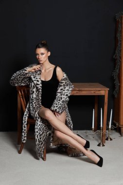 Model, kapalı alanda loş bir şekilde aydınlatılmış ahşap bir masada otururken şık bir leopar desenli ceket sergiliyor. Mumlar ve karanlık bir arka plan çekimlerin şık atmosferini arttırır..