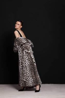 Model zarif bir şekilde etrafında dolaşan leopar desenli bir elbiseyle poz veriyor. Pürüzsüz, siyah bir arka plana karşı duruyor. Moda fotoşopu sırasında kendine güven ve tarz yayıyor..