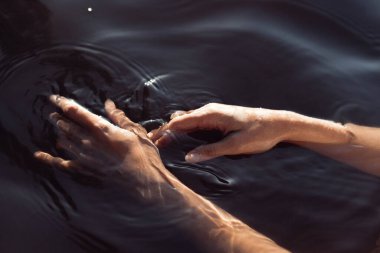 İki el, karanlık suyun pürüzsüz yüzeyiyle etkileşerek hassas dalgalanmalar ve yansımalar yaratır. Batan güneş ılık bir parıltı yayar, sakin atmosferi güçlendirir..