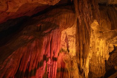 Karmaşık mağara oluşumları yerden çarpıcı bir şekilde yükselir, sıcak kırmızı ve sarılar ile yıkanır ve bu onların dokularını belirtir..