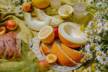 Canlı bir karpuz, şeftali ve limon gösterisi renkli çiçekler ve doğal elementler arasında gümüş bir tepside sunuluyor ve neşeli bir atmosfer yaratıyor..