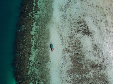 Ko Ngai adasındaki mercan resifinin oluşturduğu su altı uçurumunun yanında yüzen uzun kuyruklu teknenin havadan görünüşü ve deniz seviyesi düşük, Tayland 'ın en yüksek noktasındaki güneşli bir günde insansız hava aracı fotoğrafı.