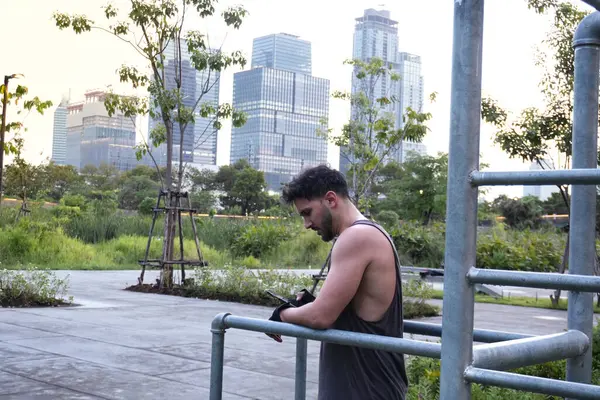 Adam gün batımında Bangkok, Tayland 'ın ortasındaki tropik bir parkta antrenman yaparken telefonunu kontrol ediyor.