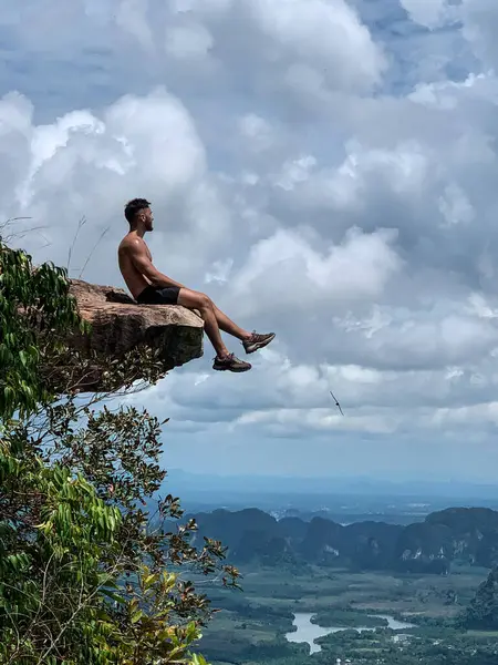 Arka planda Yengeç manzarası olan bir kayanın kenarında oturan adam.